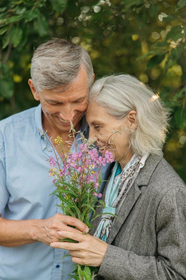 Elderly couple smiling and holding a bouquet of wildflowers together outdoors